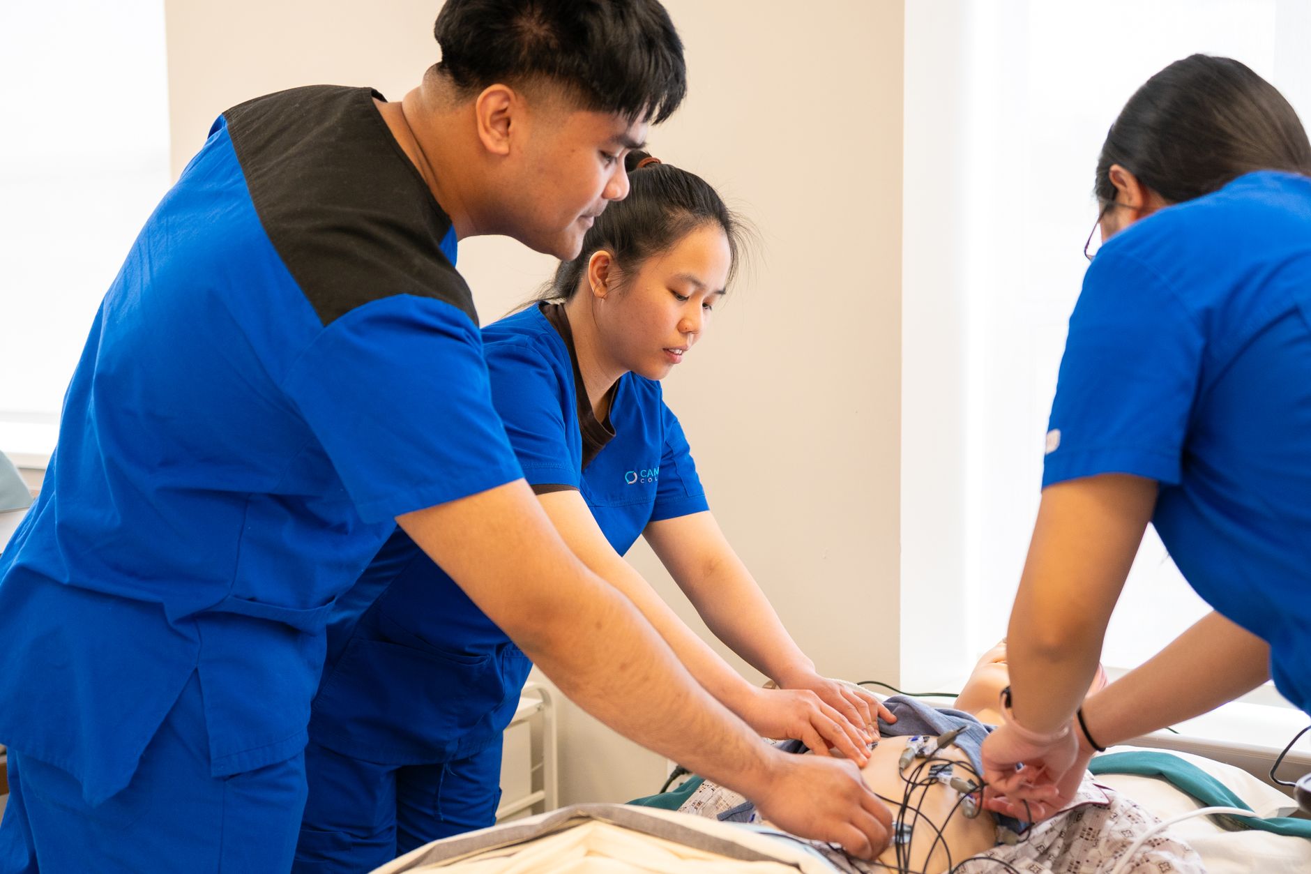 Nursing students practicing a clinical procedure on a training manikin during an ABSN skills lab