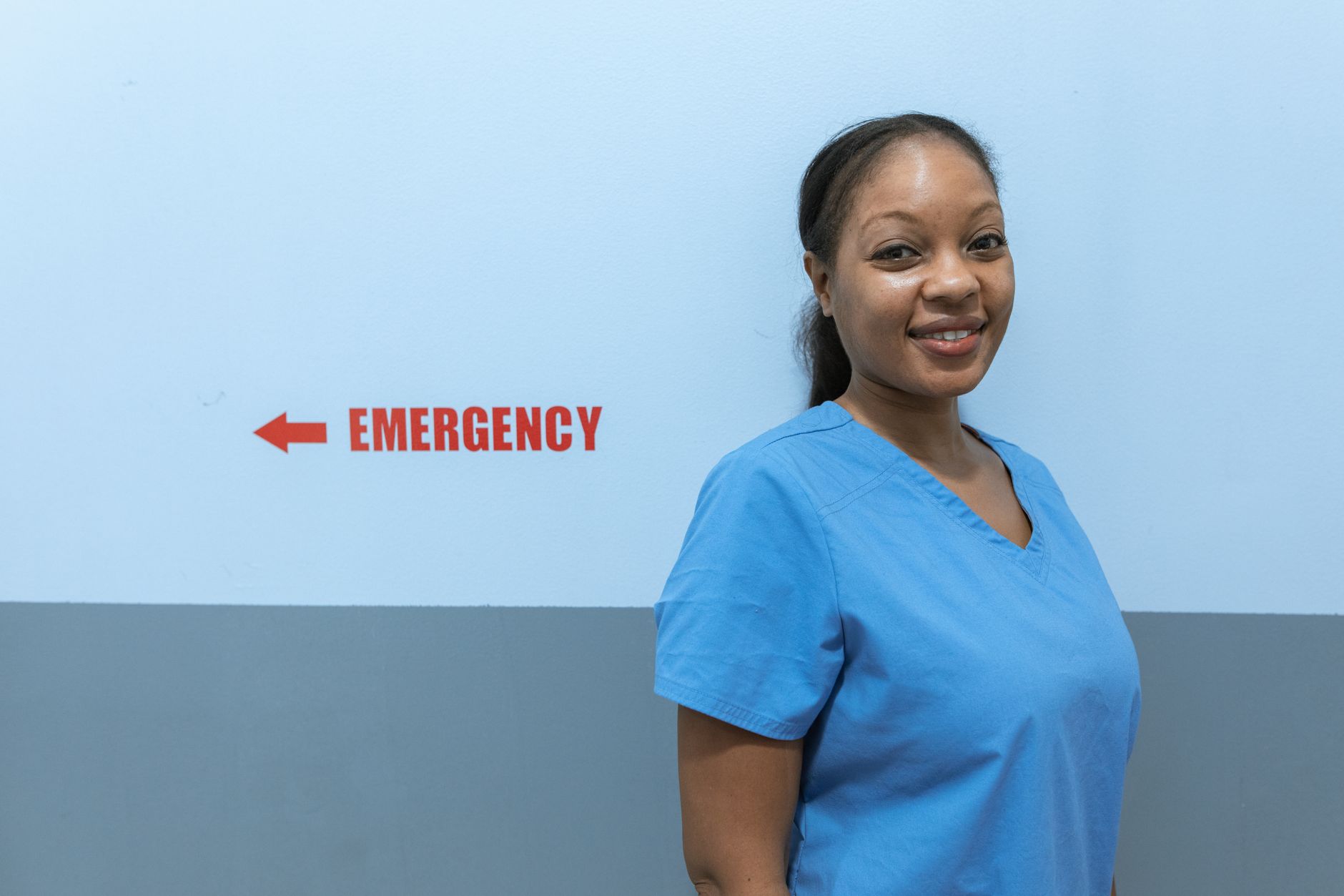 Newly licensed registered nurse in blue scrubs smiling outside a hospital emergency department