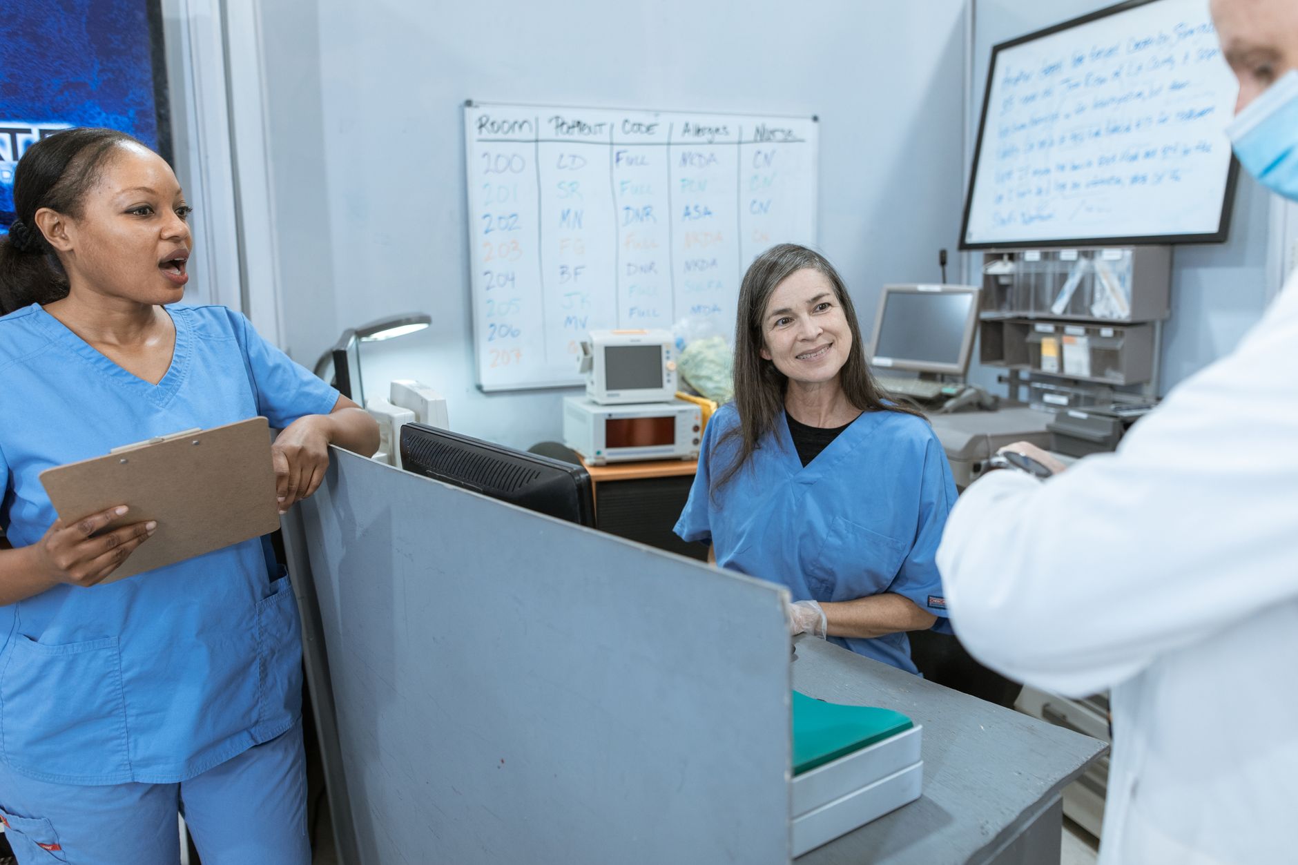 Nurses conferring at a hospital nurses station beside an assignment whiteboard, where unit culture and ratios are decided