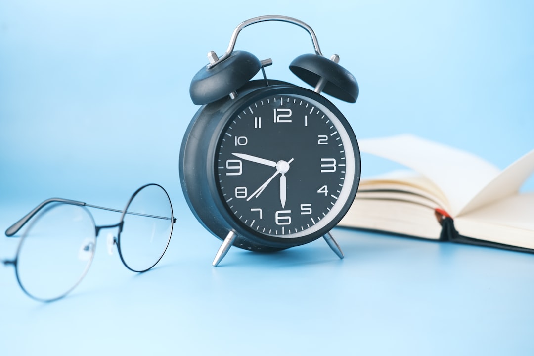 Alarm clock beside an open book and glasses, marking the CCRN's fixed three-hour, 150-item format with no early finish