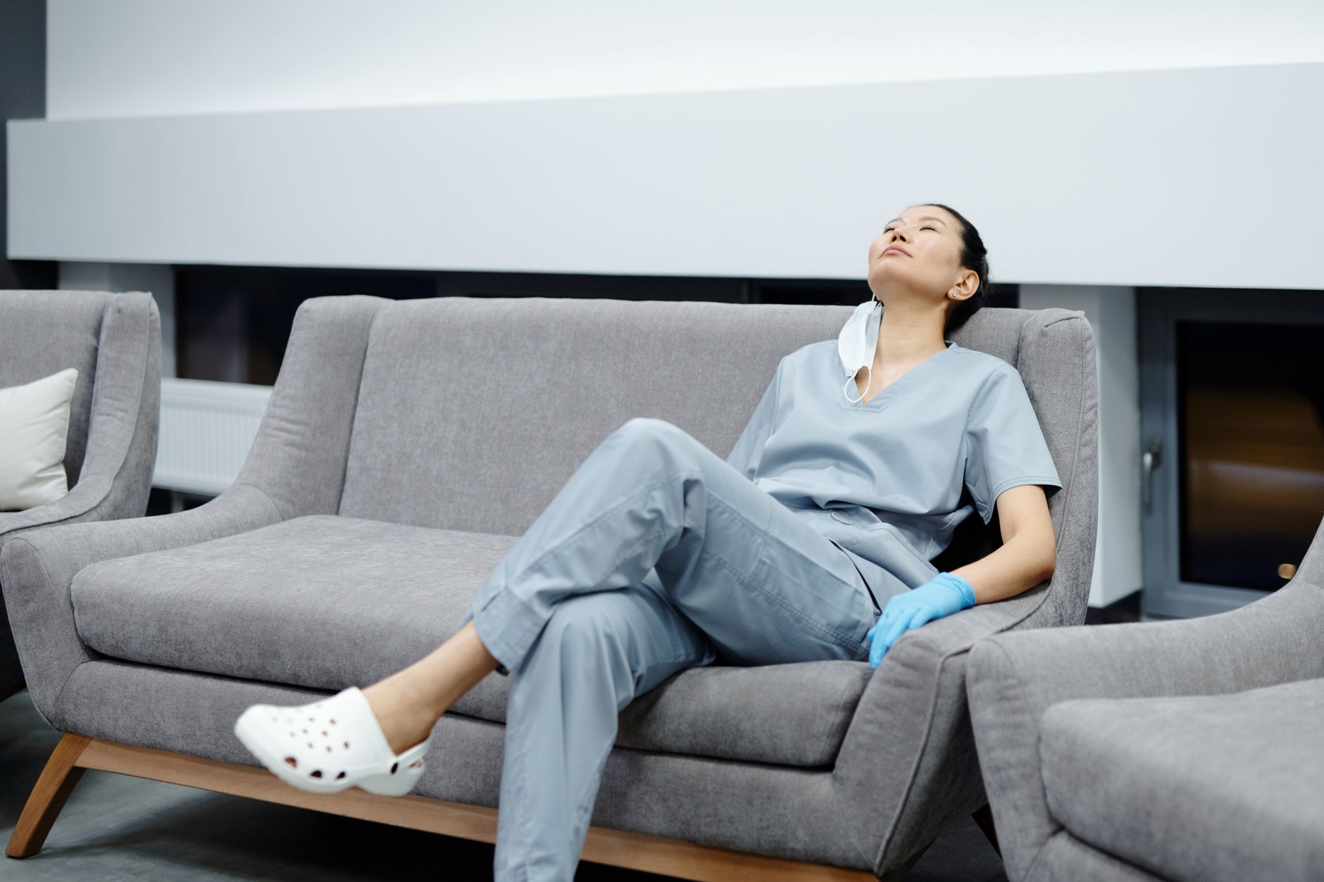 Nurse in scrubs resting on a break-room couch after a long shift, the night and weekend differentials that raise pay without changing role