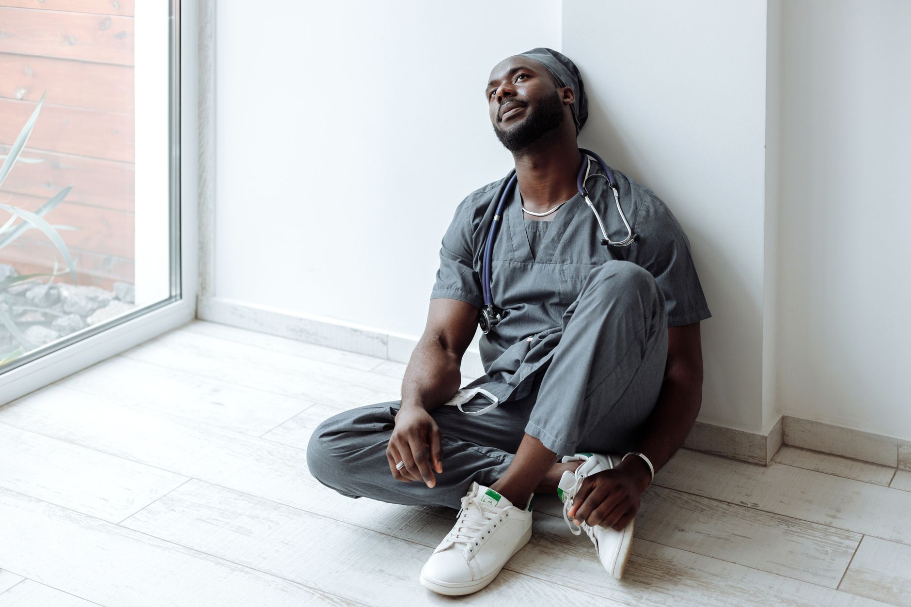 Nurse in scrubs sitting on the floor against a wall between shifts, the emotional and physical load BLS lists as a formal job requirement