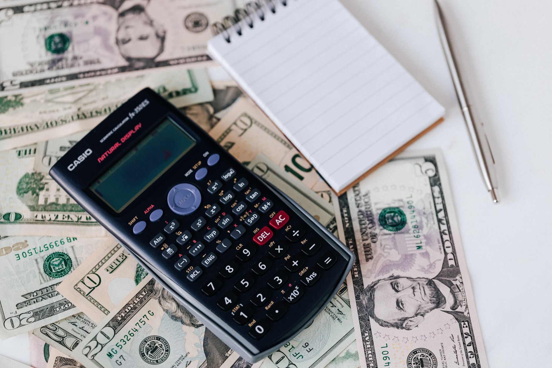 Calculator and notepad resting on US dollar bills, weighing nursing school cost against the registered nurse median wage