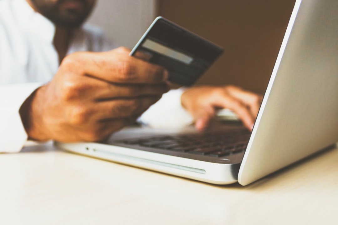 Hand holding a credit card beside a laptop during an online checkout
