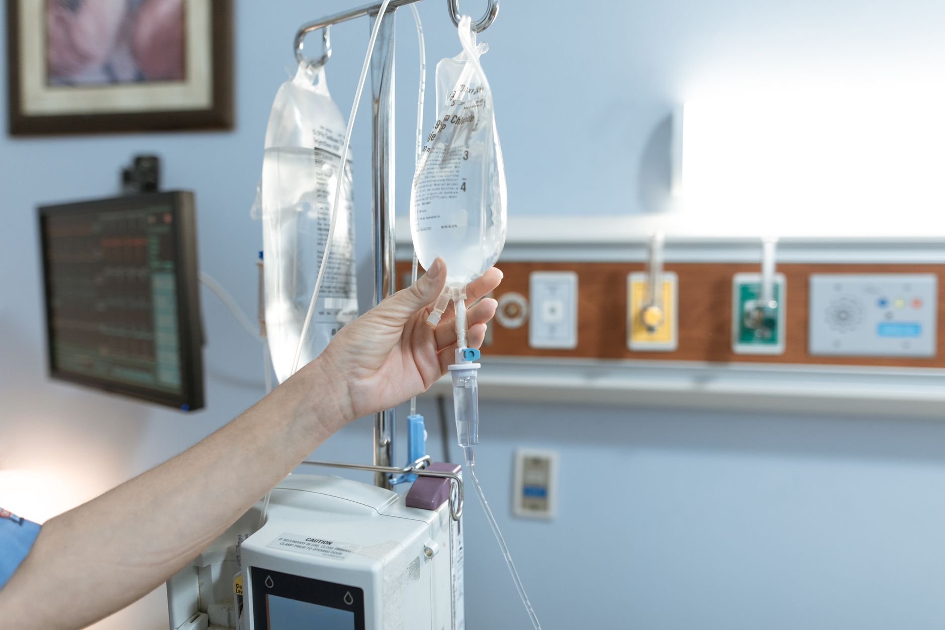 Nurse adjusting an IV infusion bag and pump at a hospital bedside
