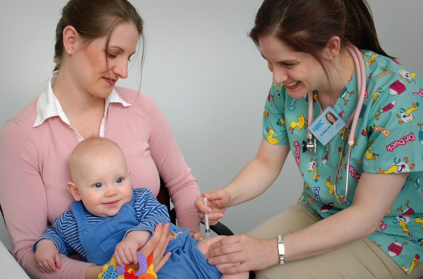 Pediatric nurse treating an infant with a parent present, the family-centred communication that runs alongside clinical care in pediatrics